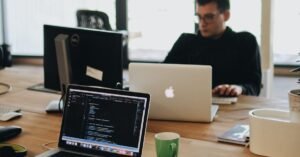 A web developer working on code in a modern office setting with multiple devices.